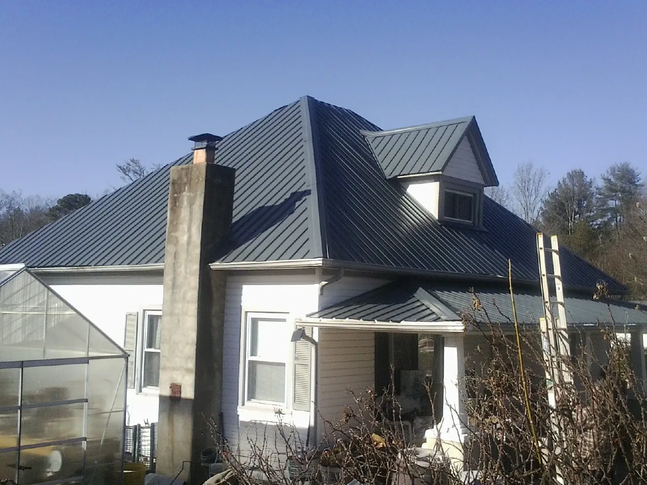 Dark blue standing seam metal roof on a white farmhouse with dormer — Slate & Tile Roof Repair by Roofing Brothers in Tenmile