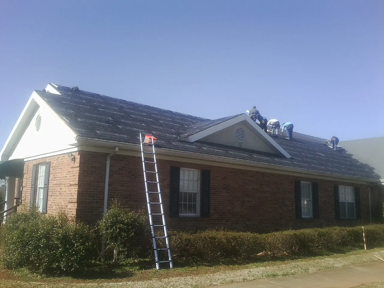 Crew tearing shingles off a brick ranch roof with a ladder set — Metal Roof Repair work by our crew in Tenmile