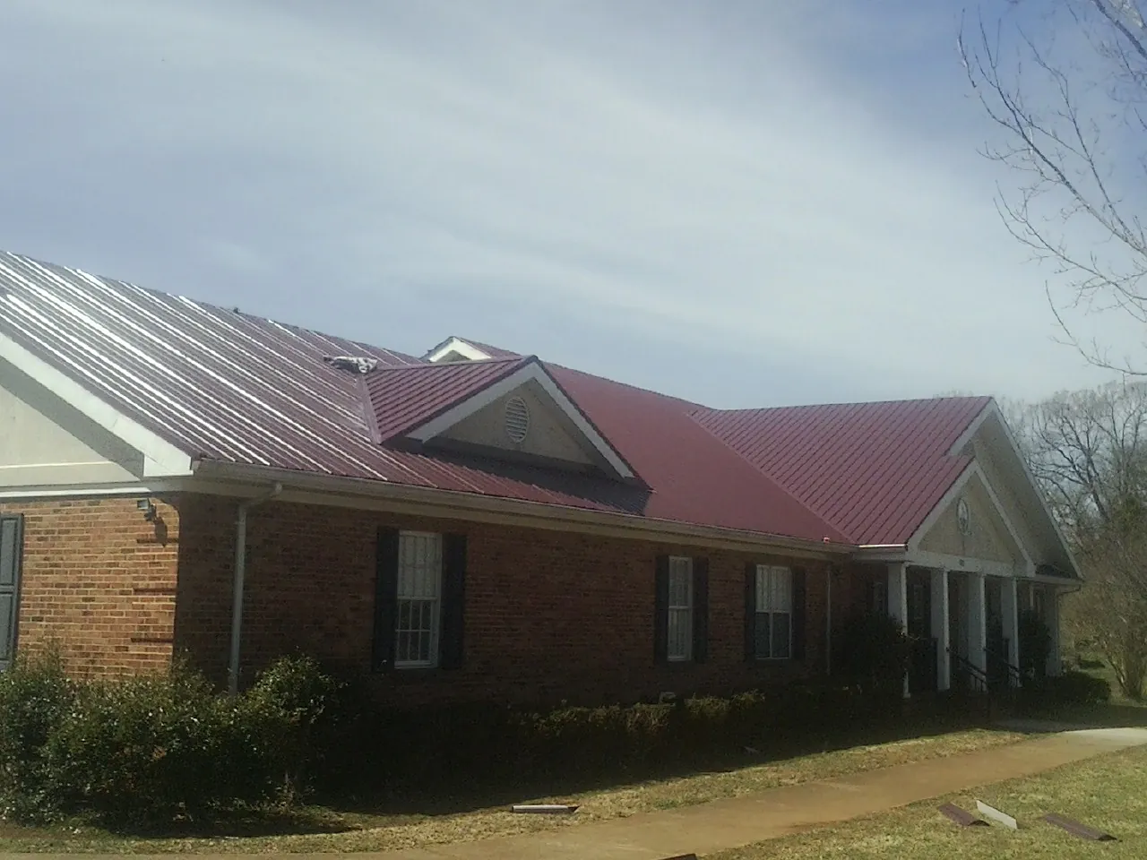 Red metal roof with gabled entries on a long brick building, from a Hail Damage Roof Repair job in Tenmile