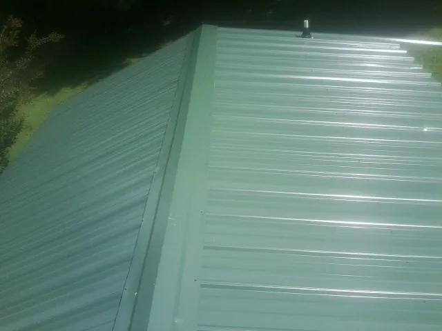 New green metal panels meeting at the ridge of a roof — Flat Roof Repair work by our crew in Tenmile