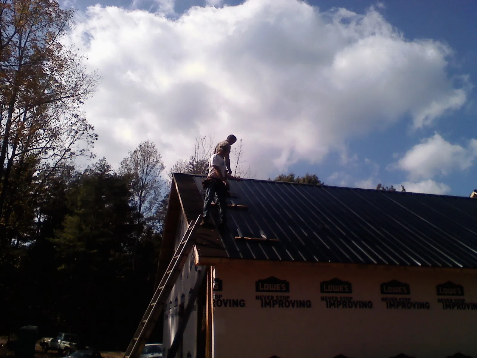 Roofer fastening dark metal panels high against a cloudy sky, from a Roof Inspection job in Tenmile