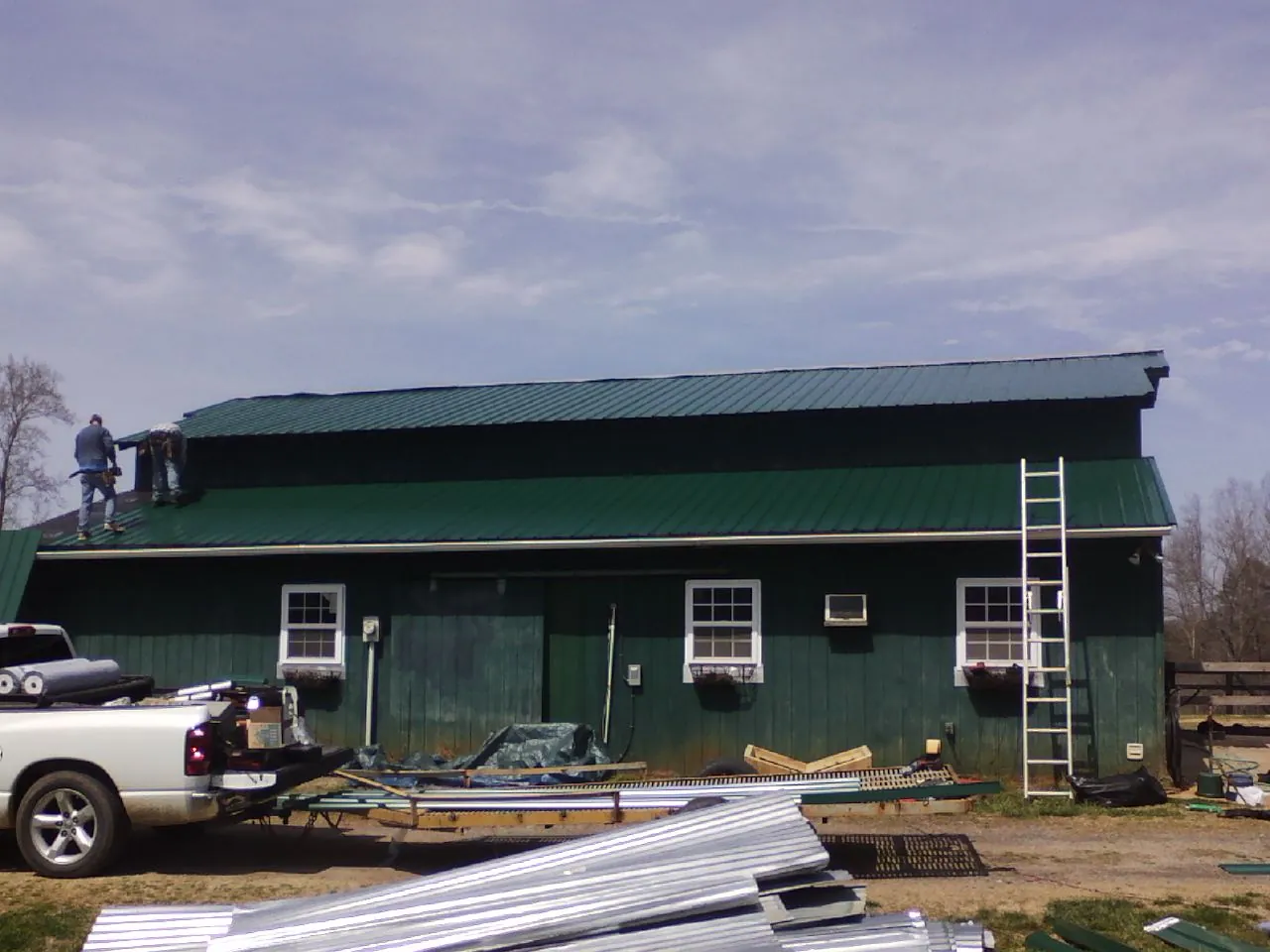 Crew installing green metal roofing on a large green barn in Tenmile