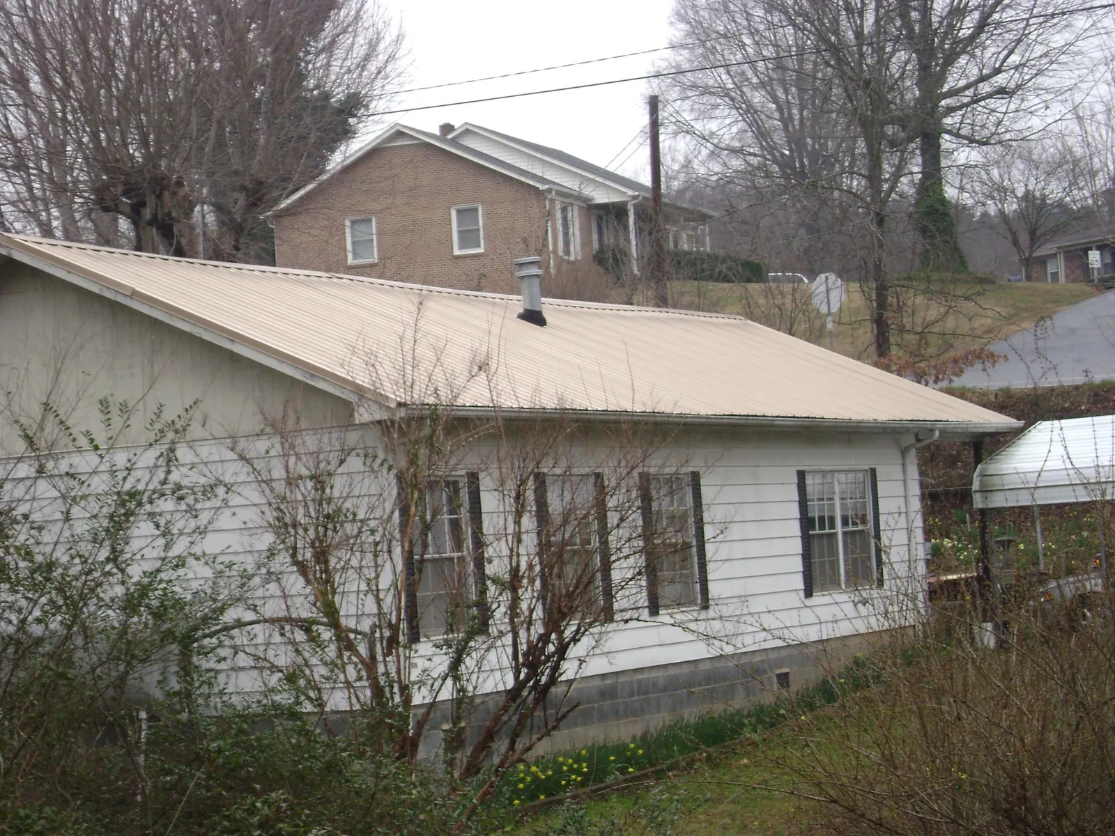 Tan metal roof on a white sided house set into a hillside — Commercial Roofing by Roofing Brothers in Tenmile