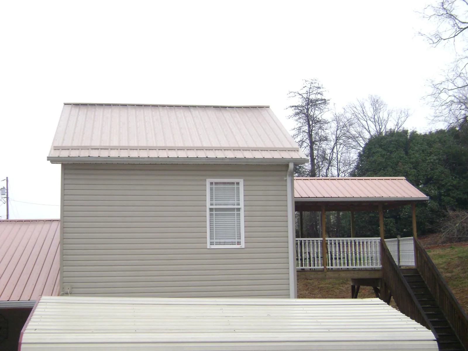 Tan metal roofs on a two story addition and attached porch, from a Roof Replacement job in Tenmile